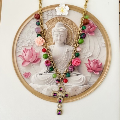 Colar dourado com pedras coloridas e cruz pendente sobre imagem de Buda e flores de lótus rosa
