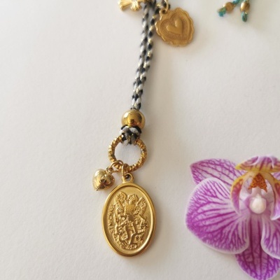 Colar com pendente dourado oval com anjos e cordão trançado preto e branco junto a uma flor orquídea roxa
