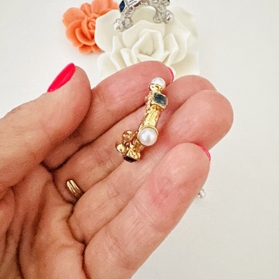 Brincos dourado e prateado com pérolas e detalhes coloridos em fundo com flores