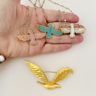 Três colares com pendentes de pássaros em contas coloridas e um broche dourado em forma de pássaro