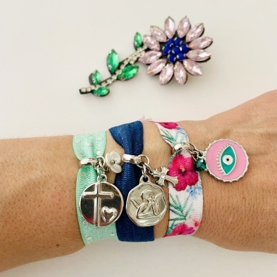 Três pulseiras de tecido elástico coloridas com pendentes metálicos usadas num pulso