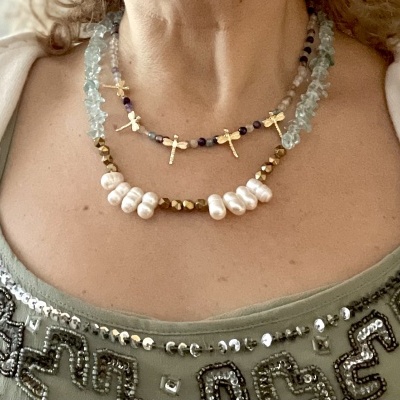 Colares com pedras azuis claras, cruzes douradas, pérolas brancas sobre camisola verde bordada.