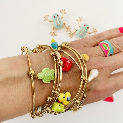 Pulseiras douradas com pendentes coloridos num pulso com anel colorido