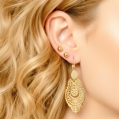 Três brincos dourados na orelha, dois pequenos e um pendente grande com padrão trabalhado