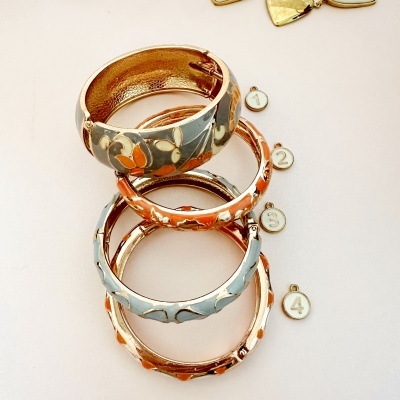 Quarteto de pulseiras douradas com esmalte colorido e padrão floral, ao lado de botões com números 1,2,3,4