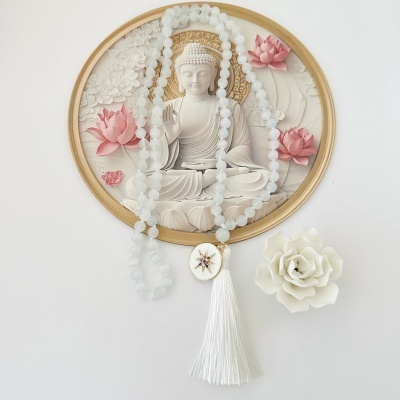Colar de contas brancas com pendente e franjas ao lado de imagem de Buda e flor branca