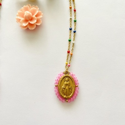 Colar com pingente religioso dourado rodeado por pedras rosas junto a conchas e uma flor decorativa.
