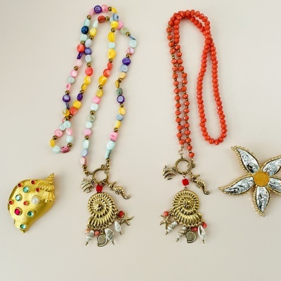 Quatro peças de bijuteria coloridas: dois colares e dois broches, sobre fundo branco.