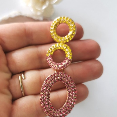 Brinco pendente com pedras amarelas e rosa em fundo branco com flor