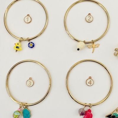 Quatro braceletes dourados com pendentes coloridos e etiquetas numeradas de 1 a 4