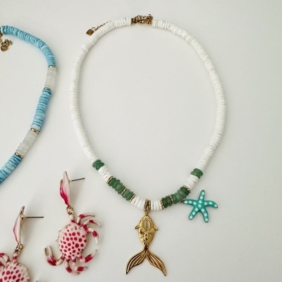 Colar branco e verde com pendentes peixe dourado e estrela do mar azul e brincos caranguejo cor-de-rosa.