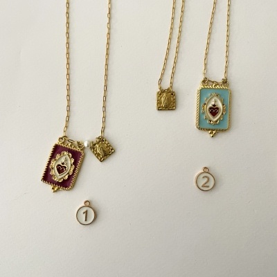 Dois colares dourados com pendentes coloridos, um bordô e outro azul claro, contra fundo branco.