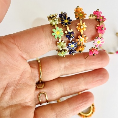 Pulseiras florais coloridas em metal dourado seguradas numa mão com anel dourado