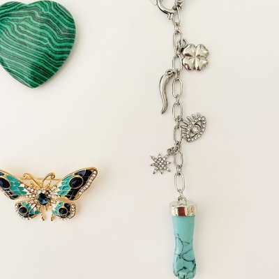 Pulseira prateada com vários pingentes e dois acessórios coloridos ao lado em fundo branco