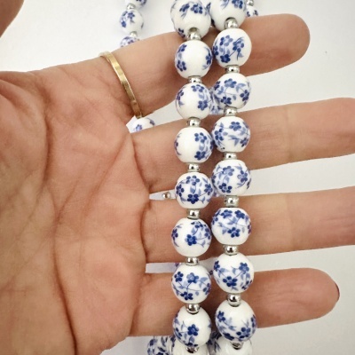 Colar com contas brancas e flores azuis segurado numa mão