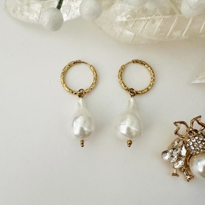 Brincos de argola dourada com pérola pendente sobre fundo branco e broche de abelha ao lado