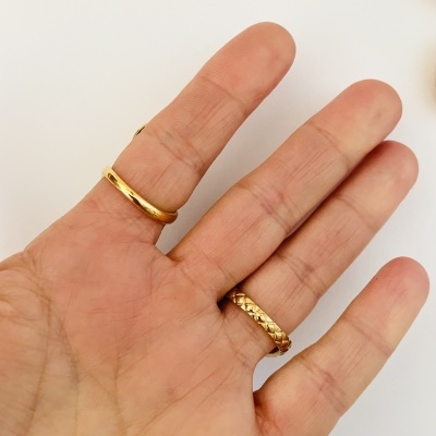 Mão com três anéis dourados, dois lisos e um trançado