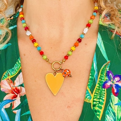 Colar colorido com pingente de coração amarelo e joaninha laranja sobre roupa verde com flores