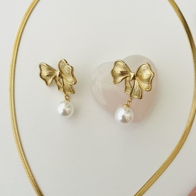 Conjunto de joalharia dourado com colar fino e brincos com laço e pérola