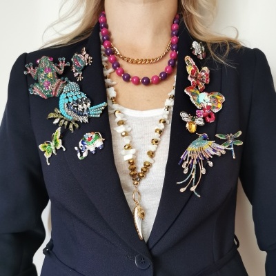 Blazer azul escuro decorado com broches coloridos e colares vistosos