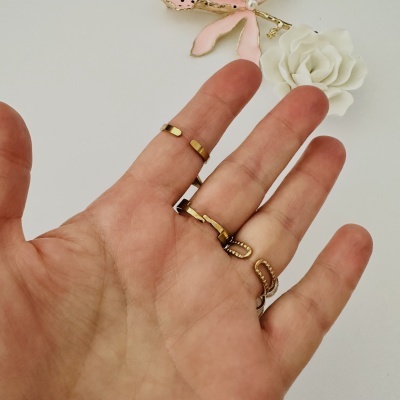 Mão com anéis dourados finos e flor branca decorativa ao fundo