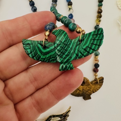Colar com pássaro verde e contas coloridas segurado por mão