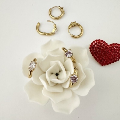 Joias douradas com pedras brilhantes, brincos de argola dourados, coração vermelho e flor branca decorativa