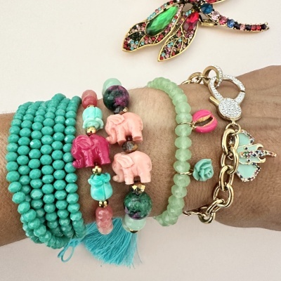 Pulseiras coloridas variadas num pulso com detalhes de elefantes, concha rosa e estrela do mar.