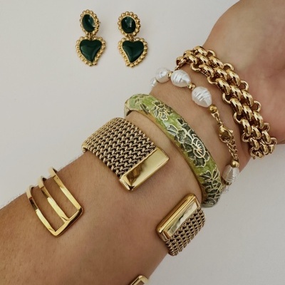 Brincos de coração verdes com contorno dourado e pulseiras variadas no pulso