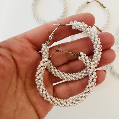 Brincos de argola com pérolas brancas em mão, fundo branco.