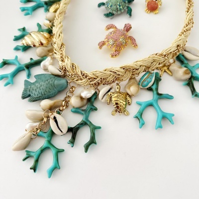 Colar com pendentes de conchas, peixes, coral, estrelas do mar e tartarugas em fundo branco.