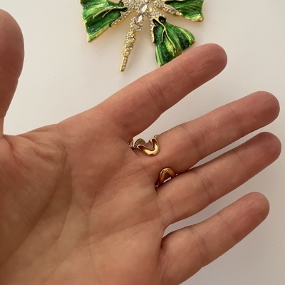 Broche trevo verde com pedras e brincos dourados em forma de coração na mão