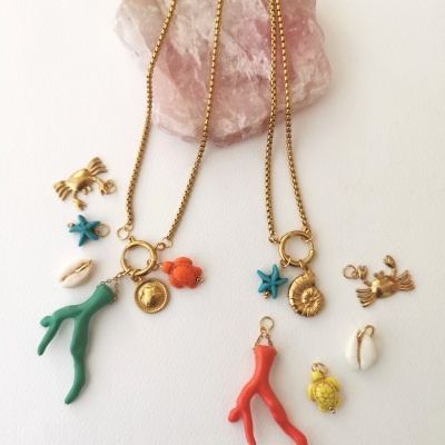 Colares com pendentes coloridos de coral, tartarugas, estrelas do mar e conchas sobre pedra rosa