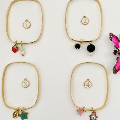 Quatro pulseiras douradas com diferentes pendentes e números de 1 a 4 em fundo branco.