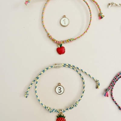 Duas pulseiras coloridas com pendentes de frutas e etiquetas numeradas