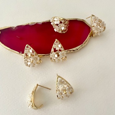 Brincos triangulares dourados com pequenas flores brancas sobre pedra vermelha