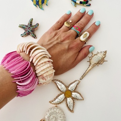 Mão com anéis e pulseiras temáticas de conchas e broches coloridos em fundo branco