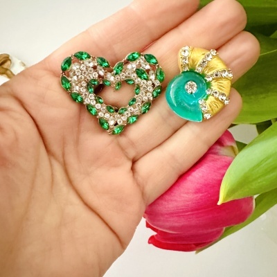 Duas broches decorativas em mão perto de uma tulipa rosa