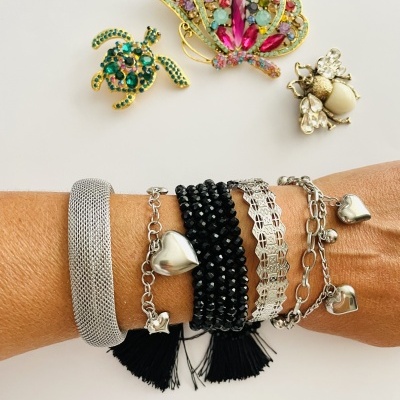 Pulseiras diversas num braço e três broches coloridos sobre fundo branco