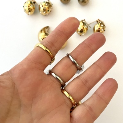 Mão com anéis prateados e dourados com brincos dourados ao fundo