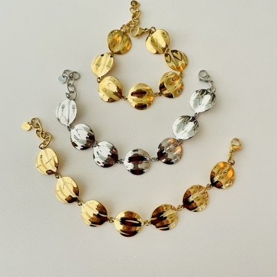 Braceletes e pulseira metálicos dourado e prateado com elos circulares sobre fundo branco