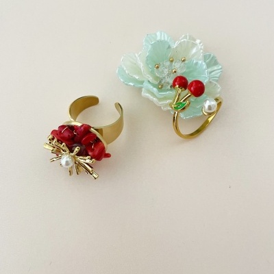 Dois anéis decorativos dourados com cores vermelho, verde-água e pérola sobre superfície branca.