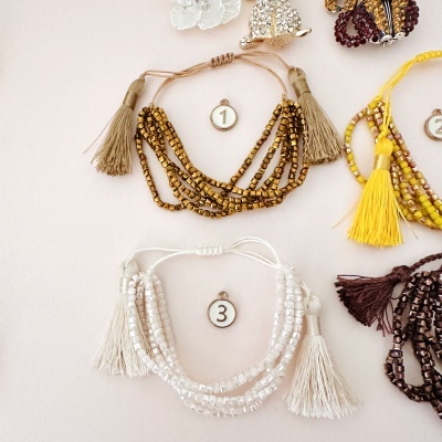 Pulseiras de contas coloridas com franjas sobre fundo claro, etiquetadas com números 1, 2 e 3