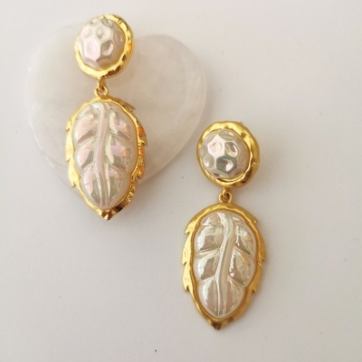 Brincos dourados com pérolas esculpidas em forma de folha sobre fundo branco com coração translúcido