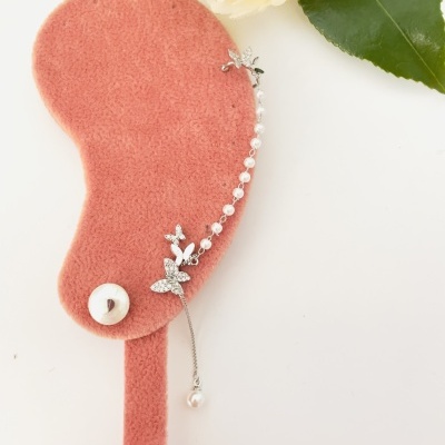 Suporte ou display de veludo rosa com pendente prateado e pérolas sobre fundo branco com flores