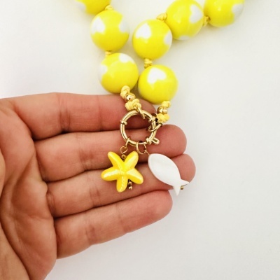Colar amarelo com contas redondas e pendentes em forma de estrela do mar e concha, próximo de uma mão