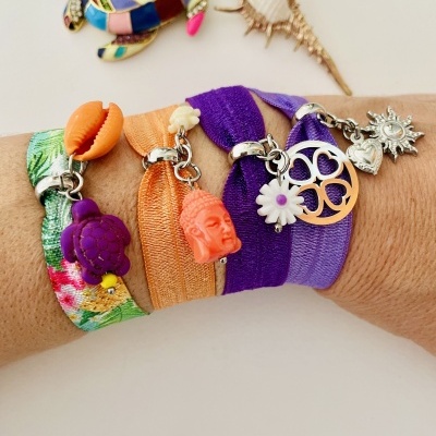 Pulseiras elásticas coloridas com pendentes variados num pulso, com broches ao fundo.
