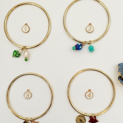 Pulseiras douradas com pendentes coloridos numeradas de 1 a 4 sobre fundo branco