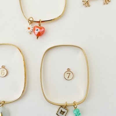 Pulseiras douradas com pendentes coloridos e etiquetas numéricas