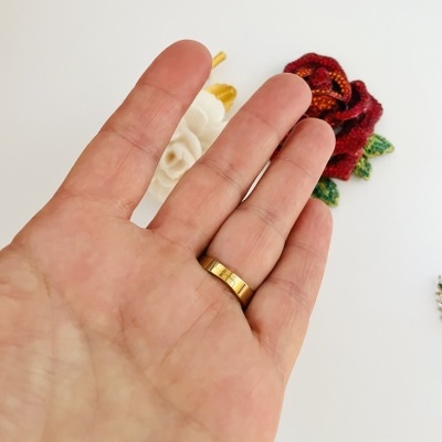 Mão com anel dourado e flores bordadas ao fundo